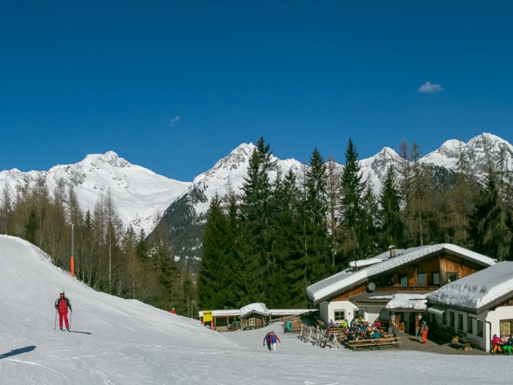 Skihütte vor der verschneiten Bergkulisse.